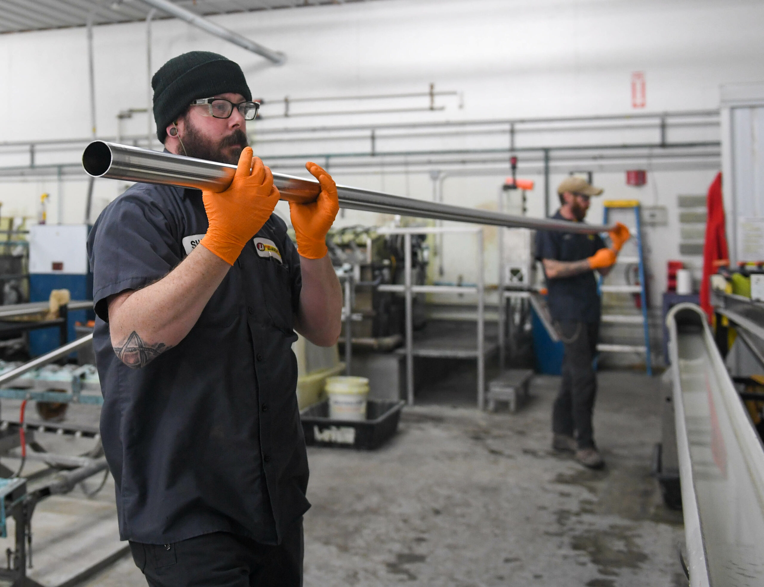 2 men working together to carry a long pipe